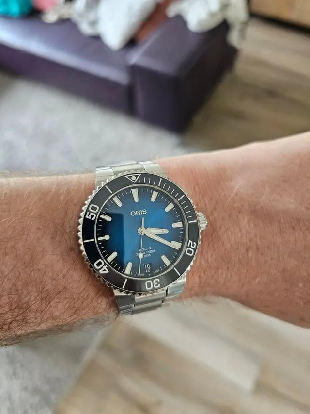 Oris Aquis blue dial on steel bracelet worn on wrist, indoor setting.