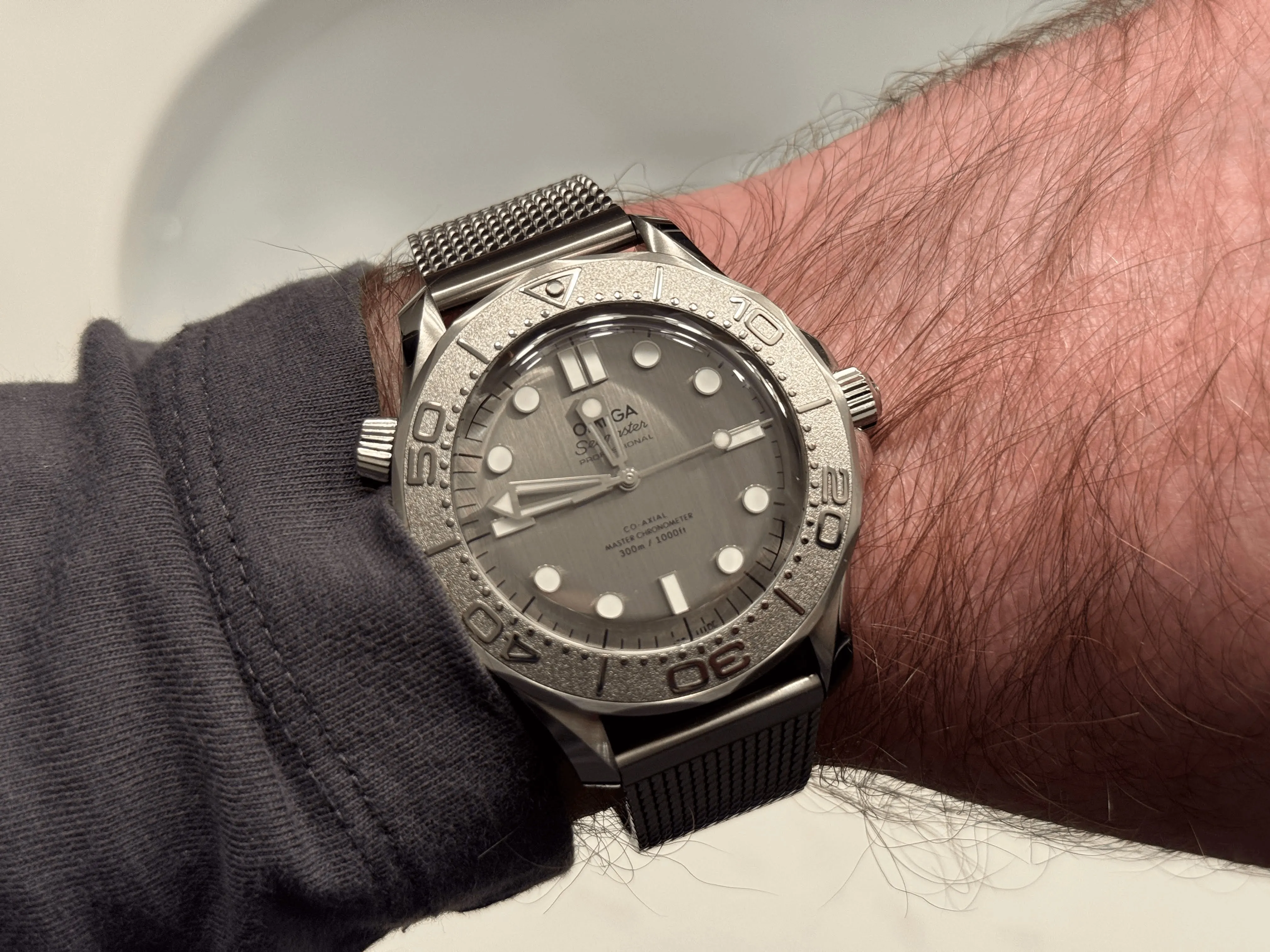 Omega Seamaster 300m on wrist, sandblasted grey ceramic bezel, grey dial, mesh bracelet.