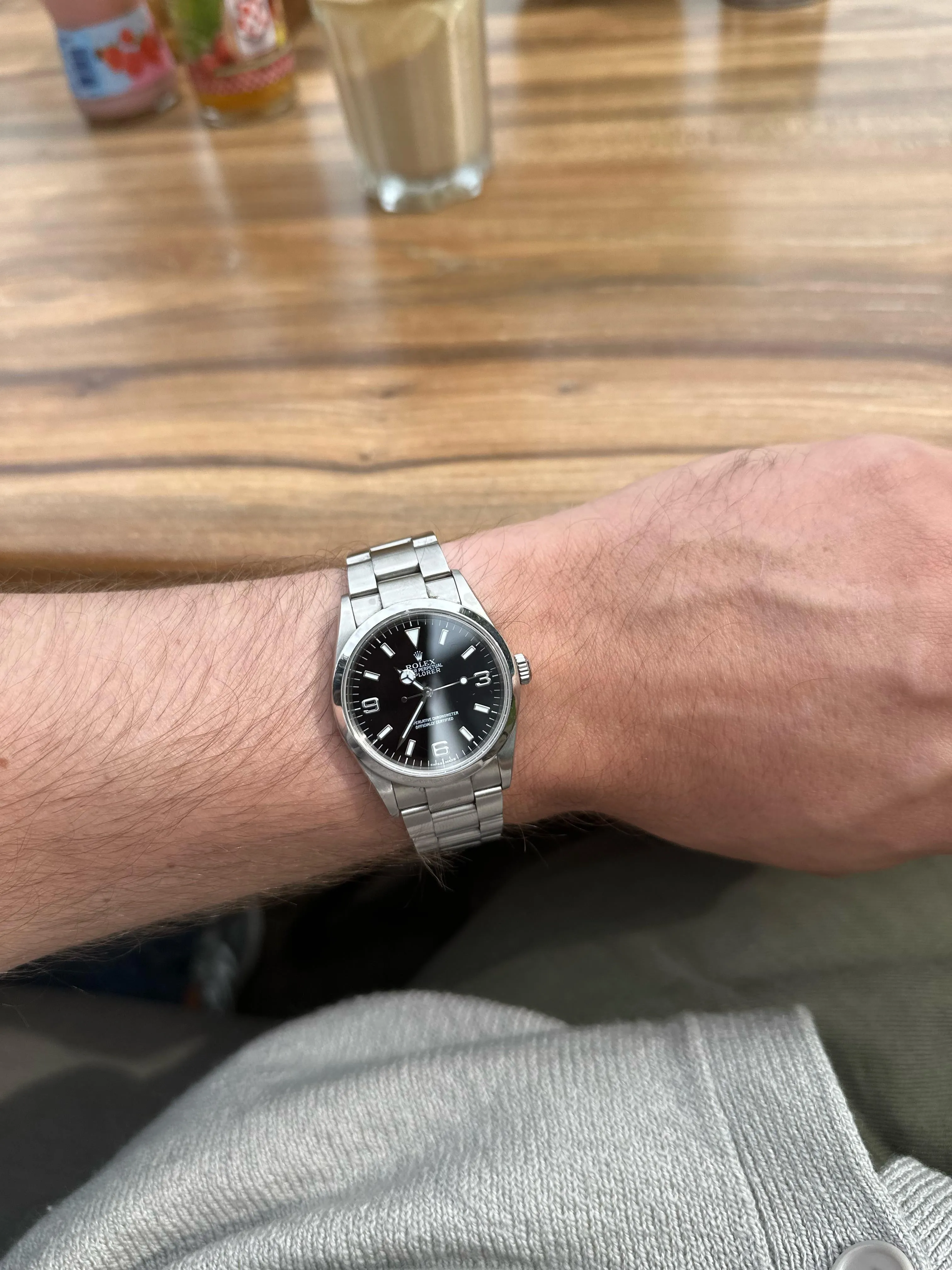 Rolex Explorer black dial on wrist with Oyster bracelet, casual café setting