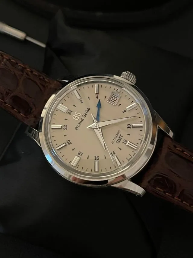 Grand Seiko SBGM221 on dark surface showing polished case and cream GMT dial