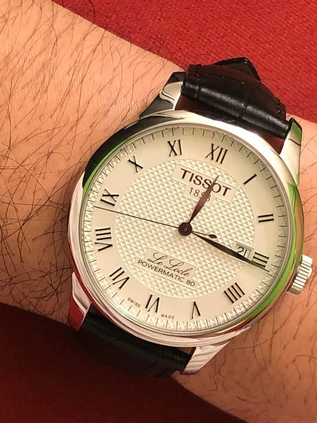 Tissot Le Locle Powermatic 80 on brown leather strap, worn on wrist, red background