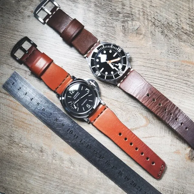 Two leather watch straps with patina and colour variation laid flat on wood surface