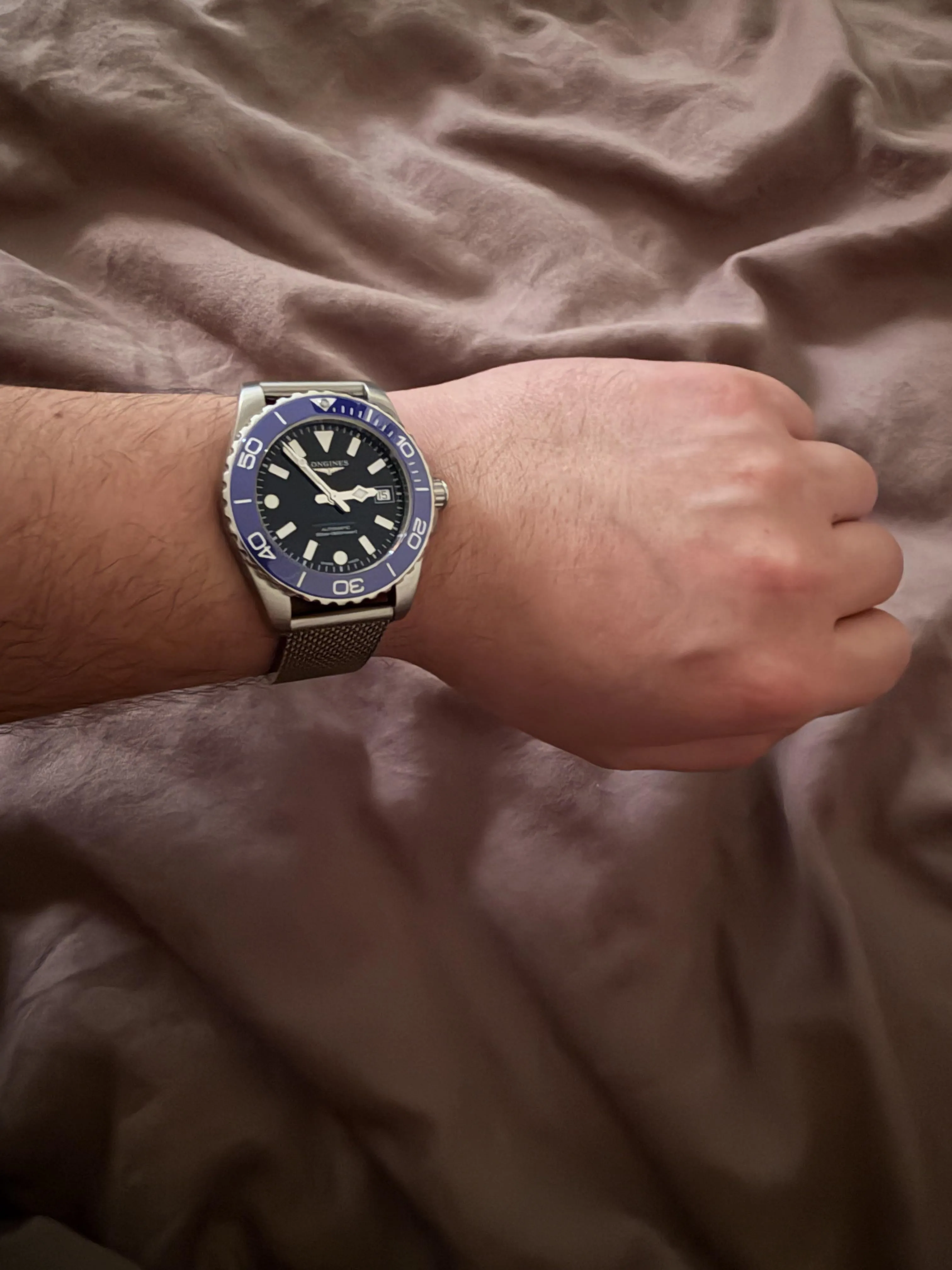 Longines HydroConquest 39mm blue bezel on wrist, steel mesh bracelet, grey background