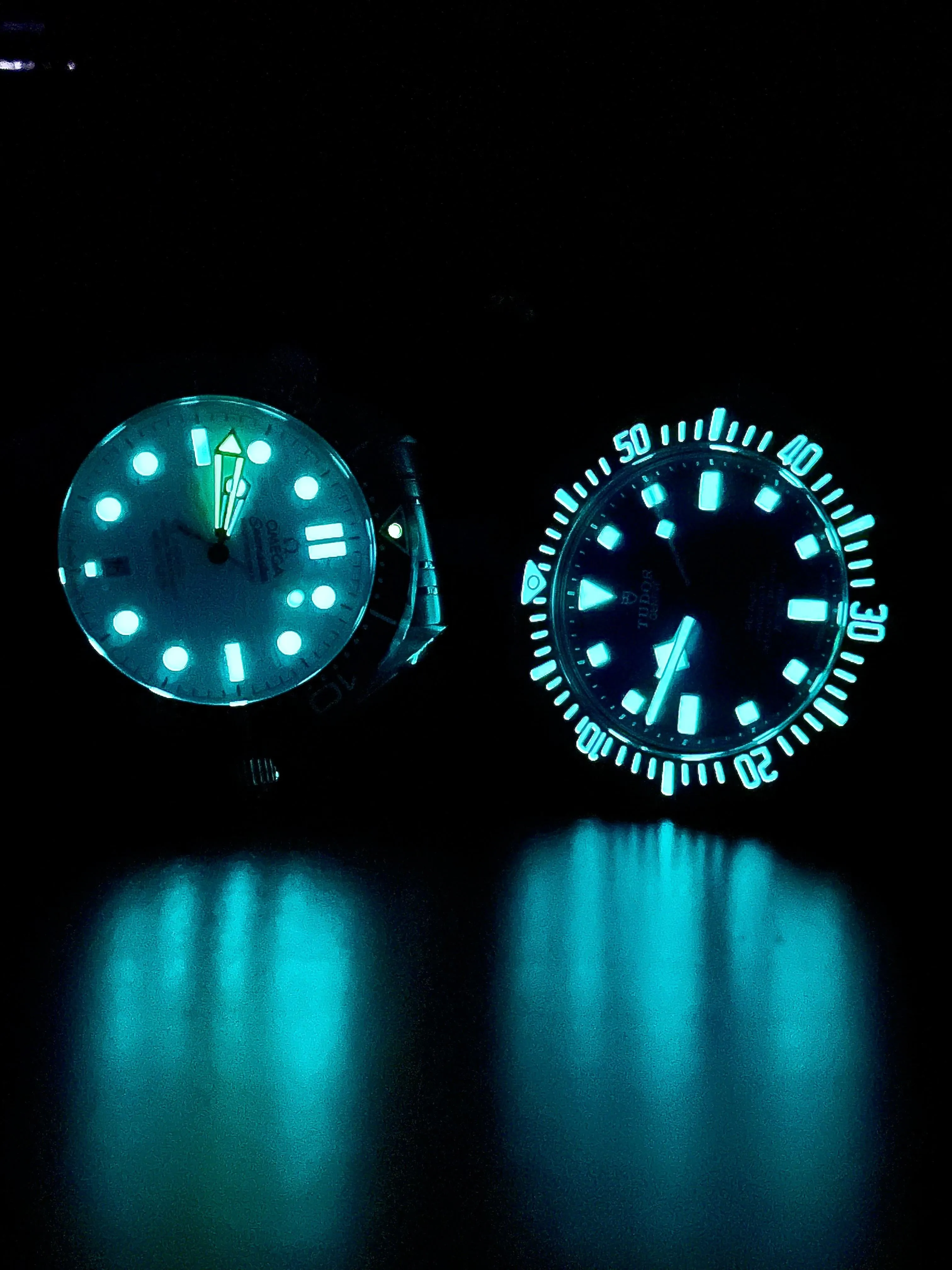 Two glowing watch dials in the dark; left shows green hands vs blue-white dots, right glows uniform cyan.