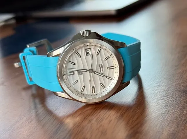 TAG Heuer Aquaracer with white wave dial on cyan FKM rubber strap, flat-lay