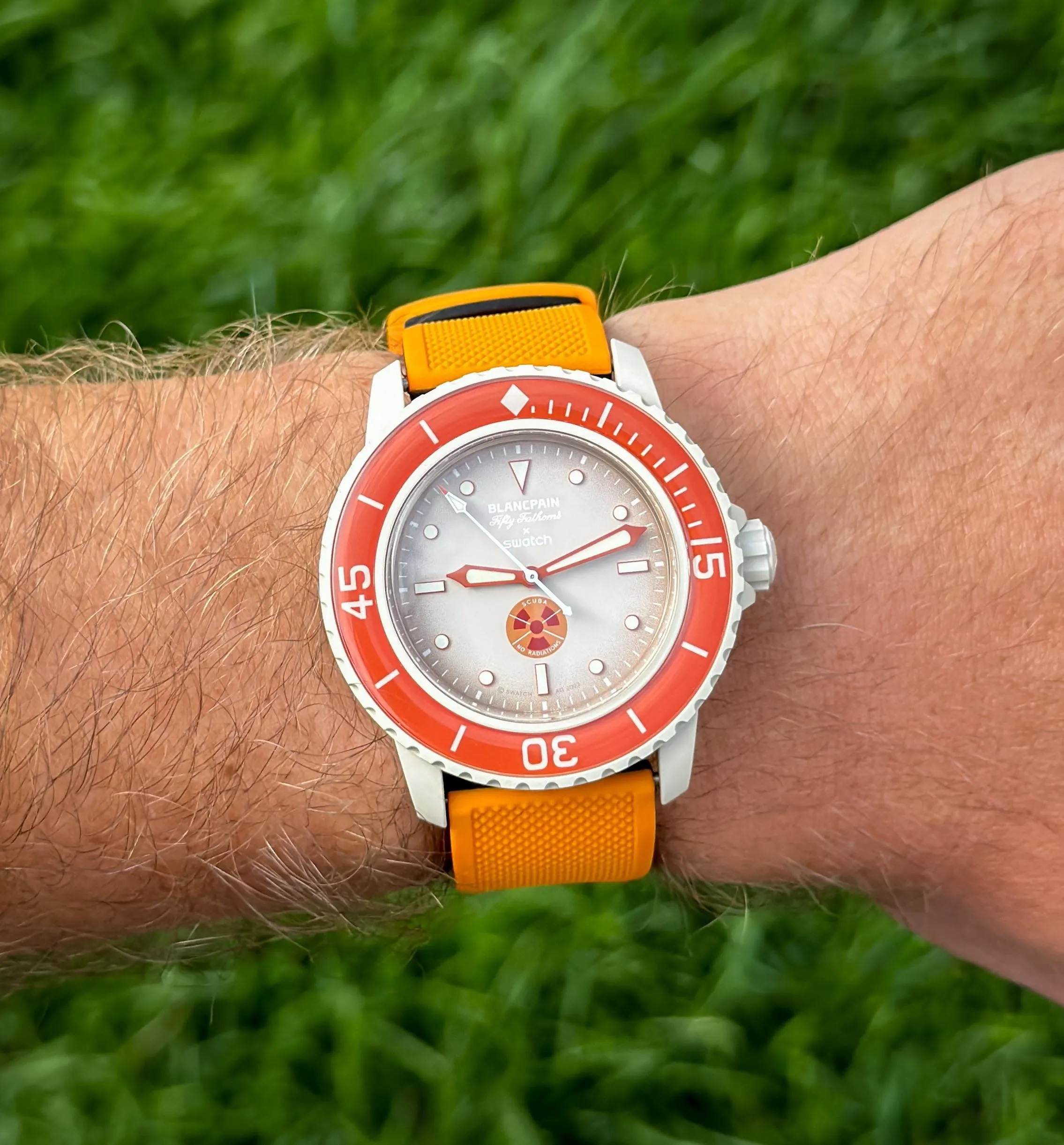 Blancpain x Swatch Fifty Fathoms on orange strap worn on wrist over green grass