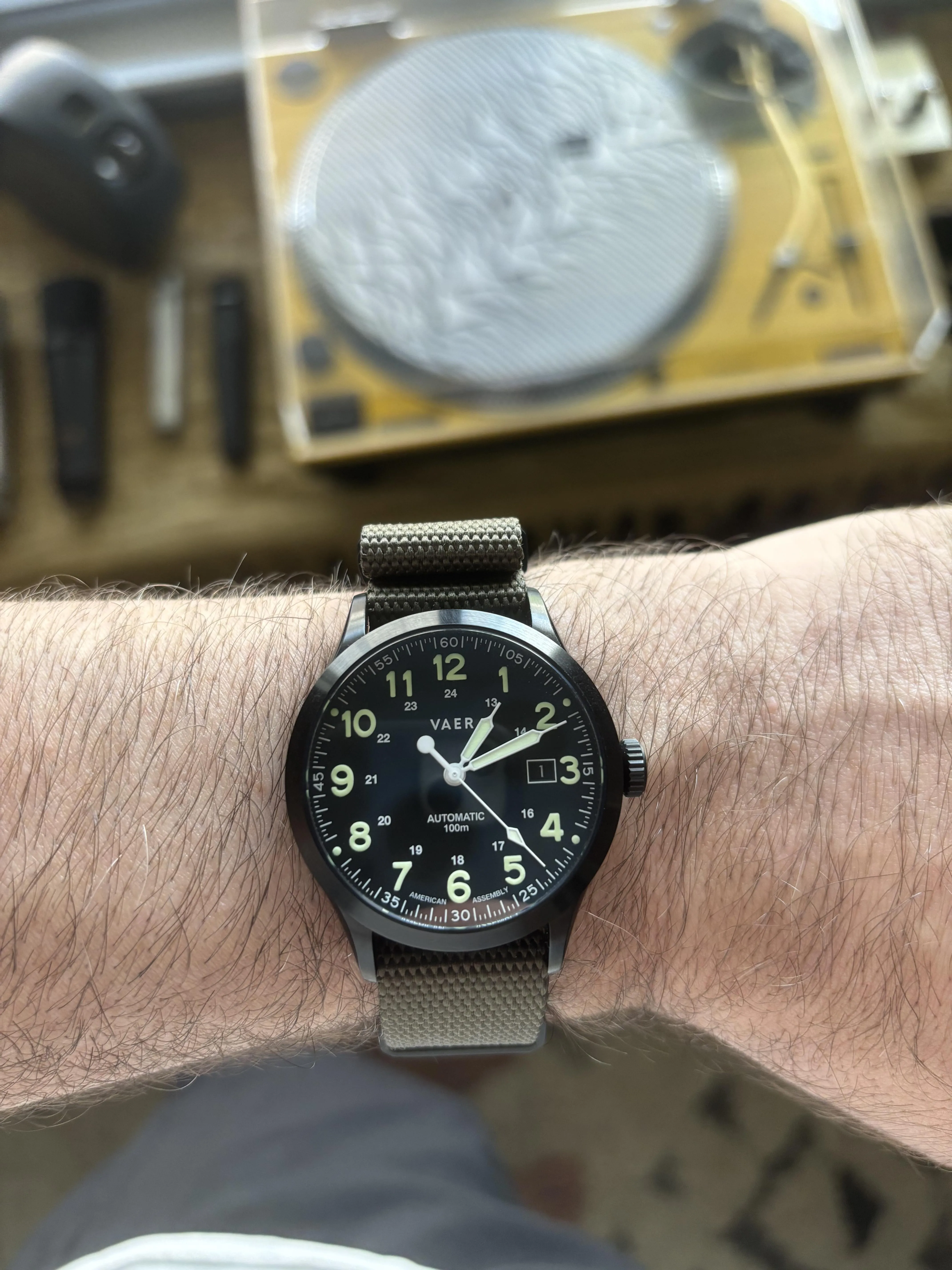 VAER field watch on olive NATO strap, double-layer nylon threading under case clearly visible.
