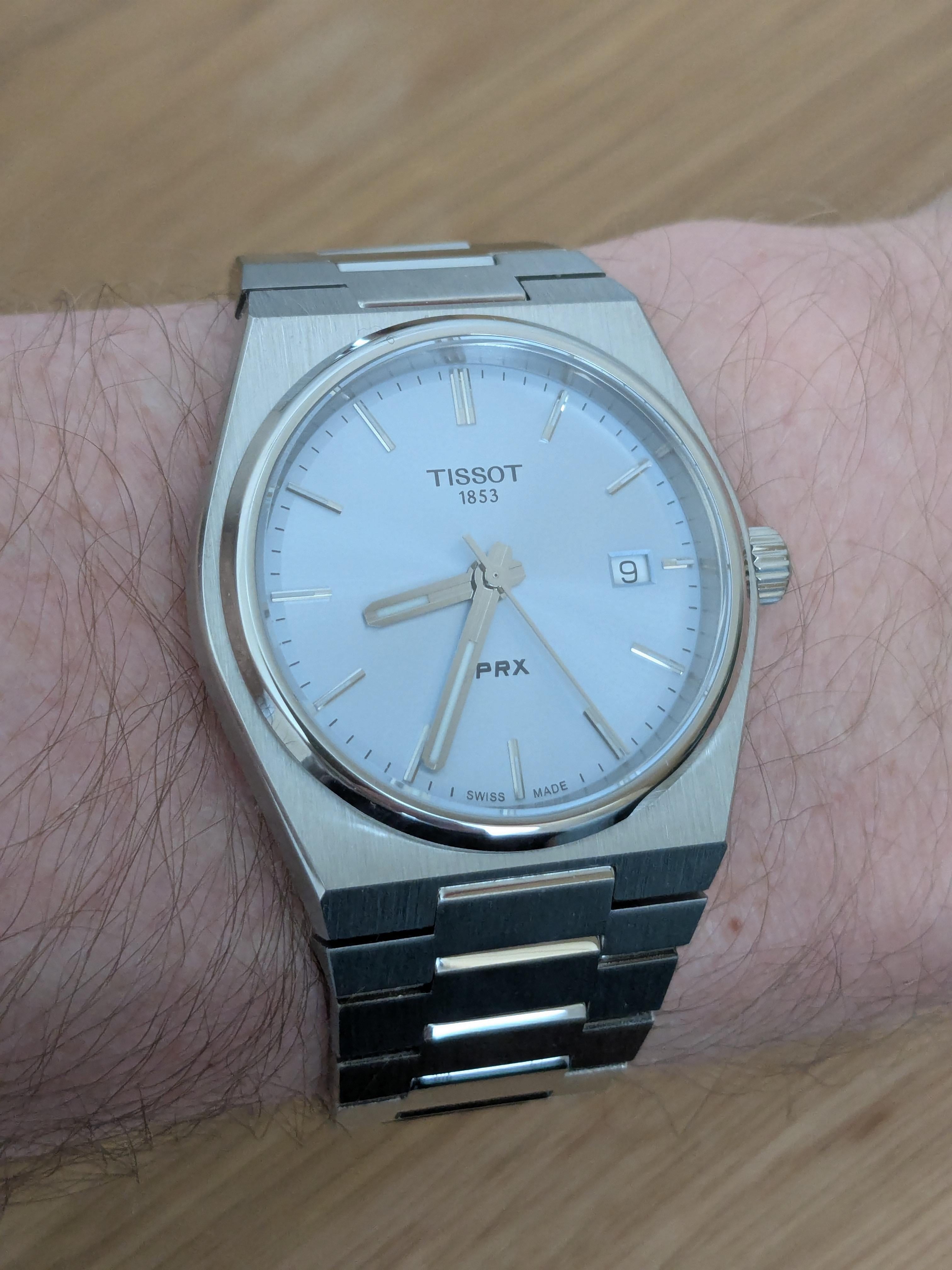 Tissot PRX white dial on wrist, stainless steel integrated bracelet, three-quarter view.