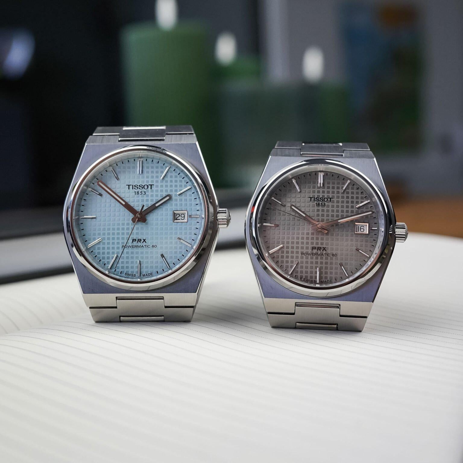 Two Tissot PRX Powermatic 80 watches, ice-blue and grey dials, on desk