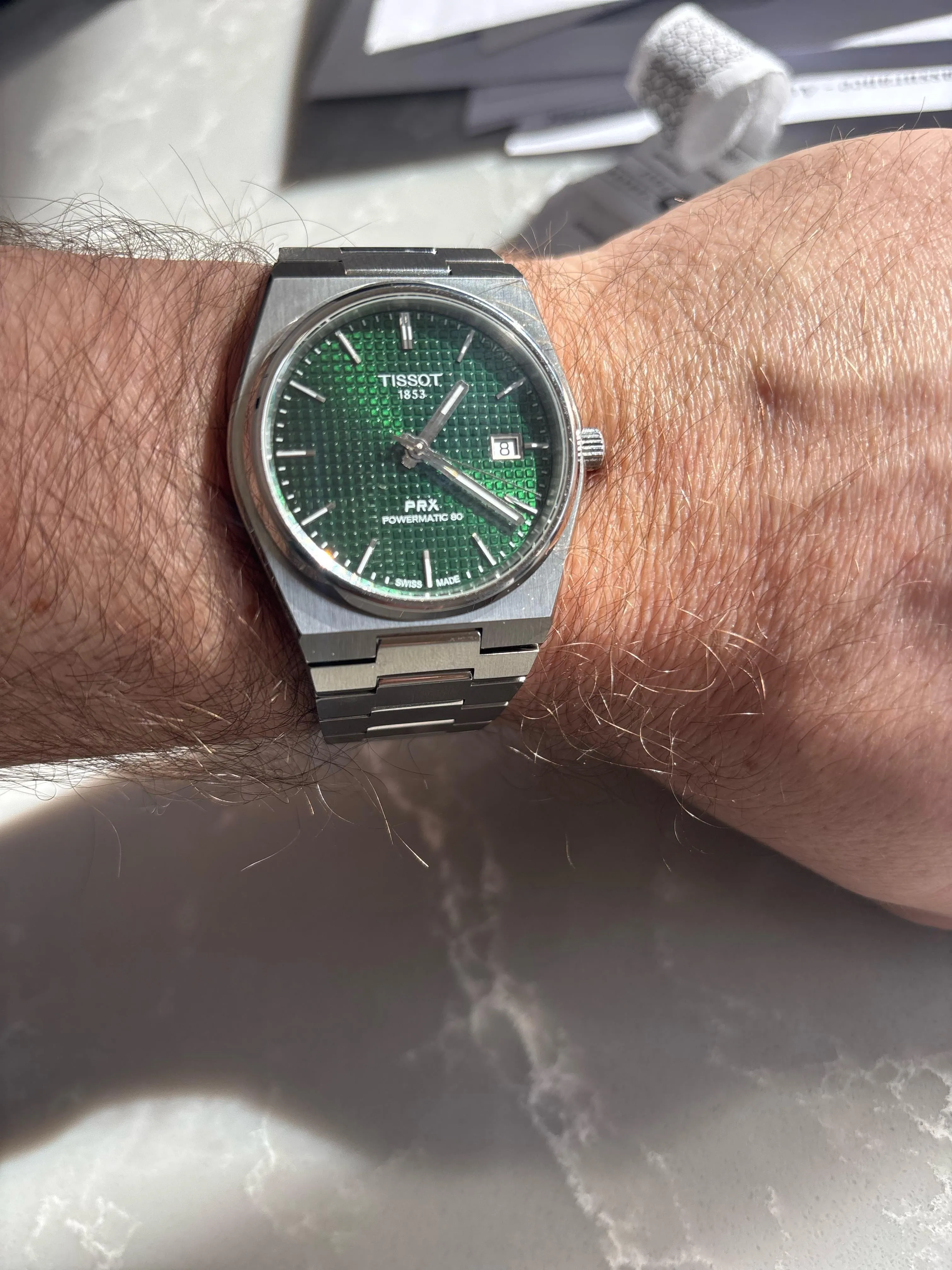 Tissot PRX 40mm green waffle dial on wrist over marble surface