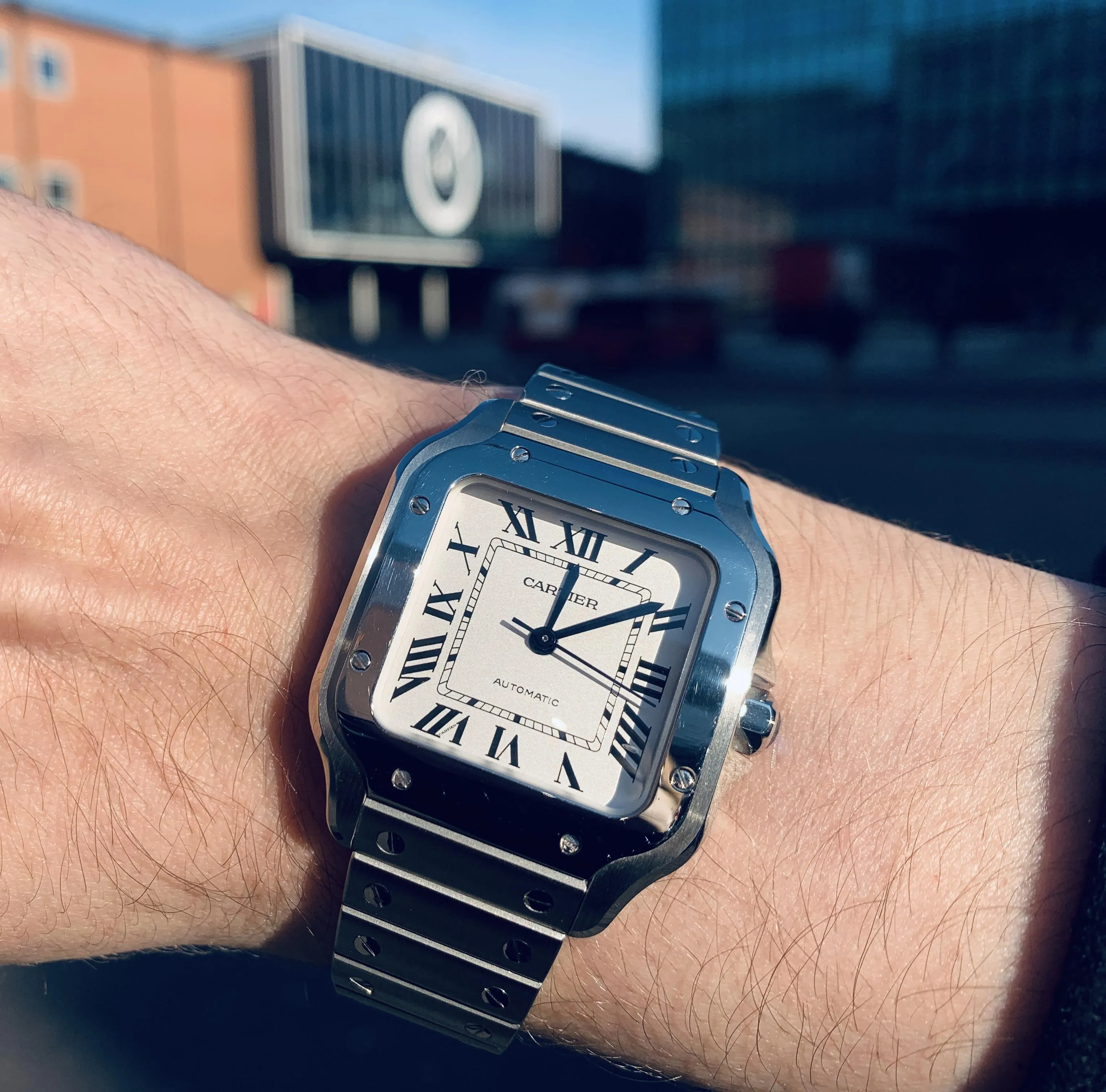 Cartier Santos white dial, screw-set bezel, blue hands, bright natural light, urban backdrop