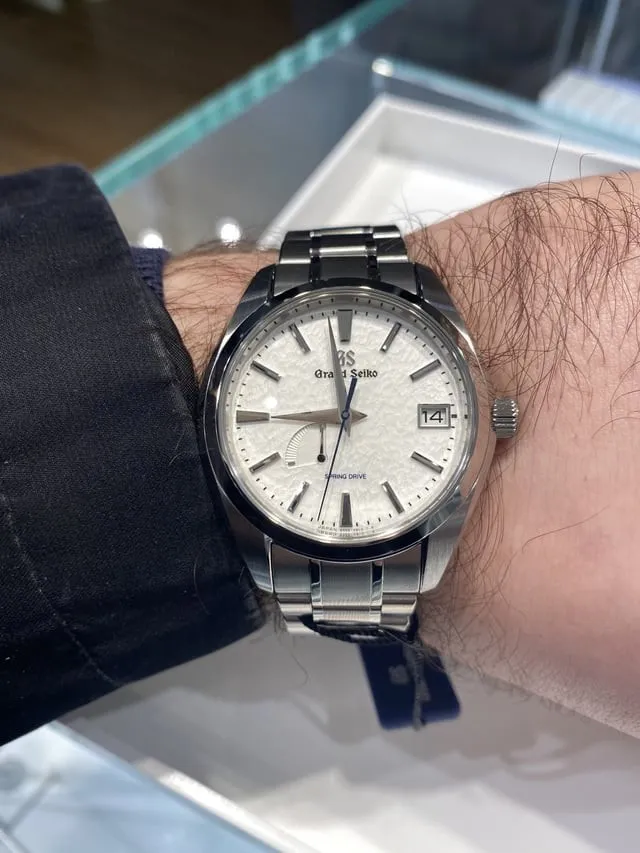 Grand Seiko Snowflake on steel bracelet worn on wrist, white textured dial visible.