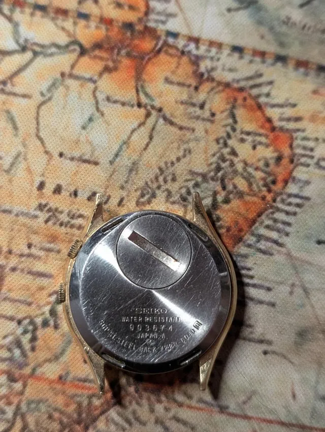 Solid Seiko screwback caseback engraved with brand text and serial number on vintage map