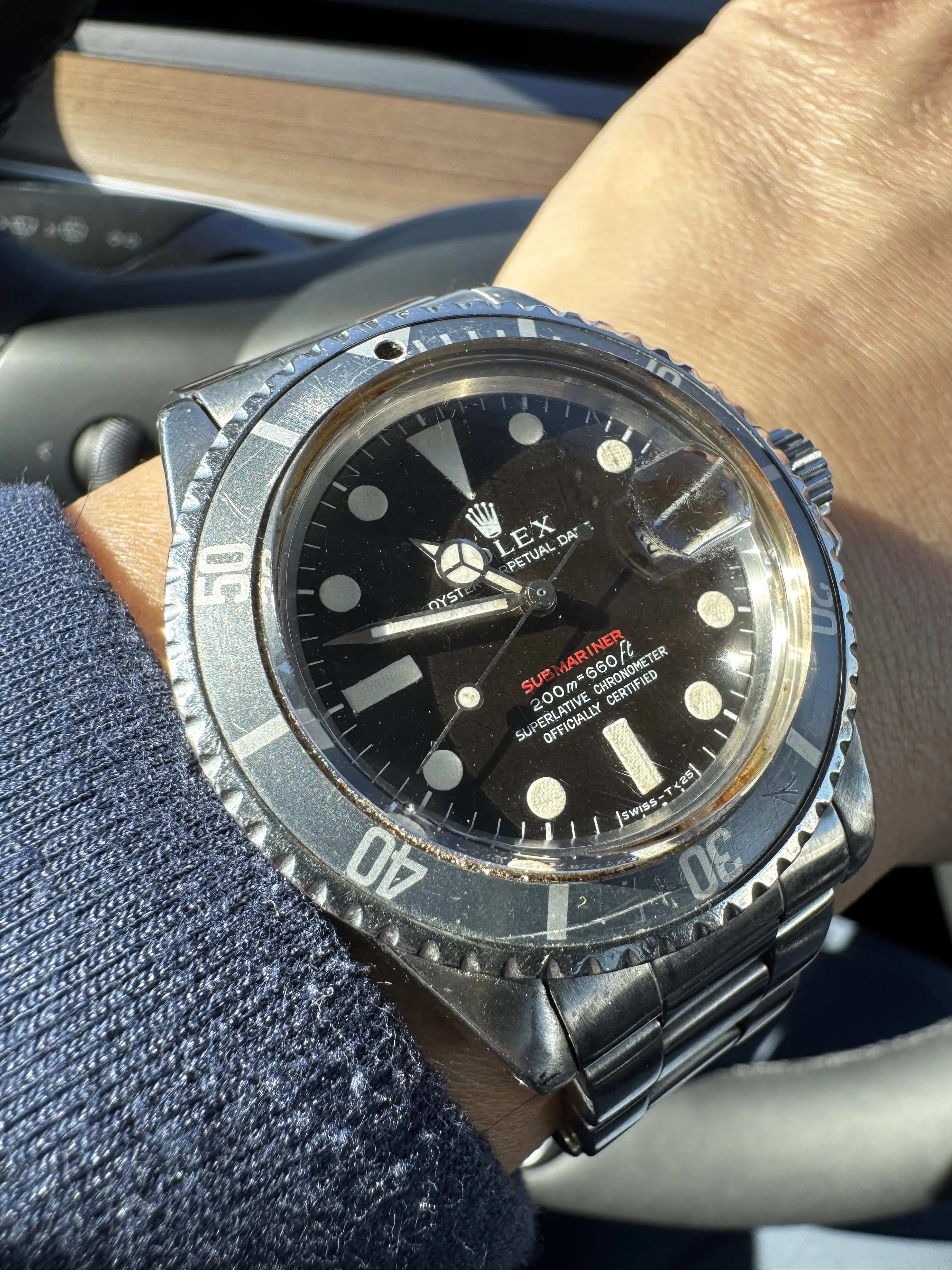 Vintage Rolex Red Submariner no-date on wrist over navy sleeve inside a car.
