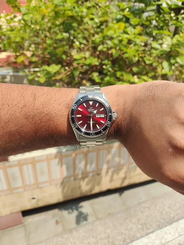 Orient Kamasu red sunburst dial on wrist, radial brushing and colour shift visible