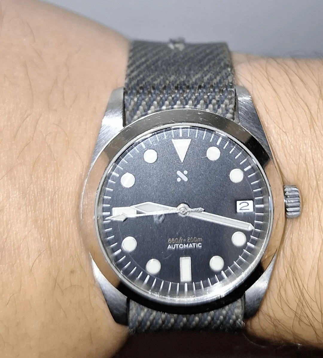 Dark dial field/diver watch with sword hands and lume dot indices on grey NATO strap