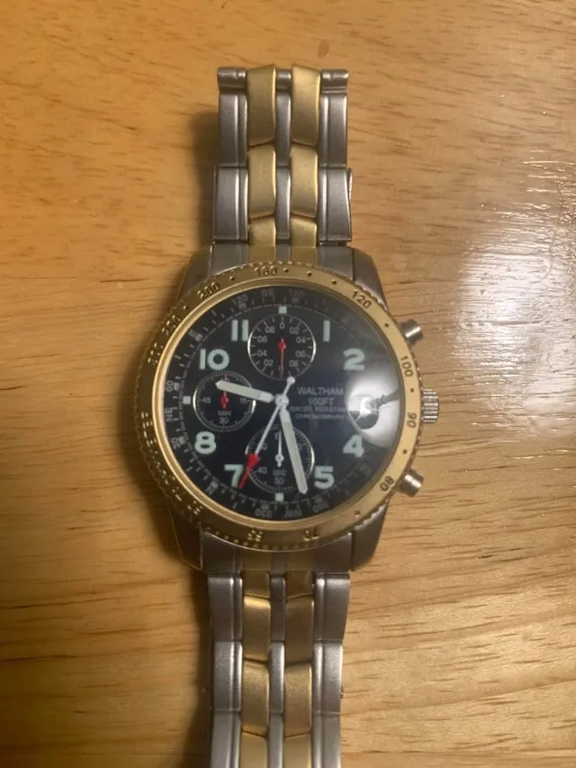 Waltham chronograph with gold-tone tachymeter bezel on stainless bracelet, flat-lay.