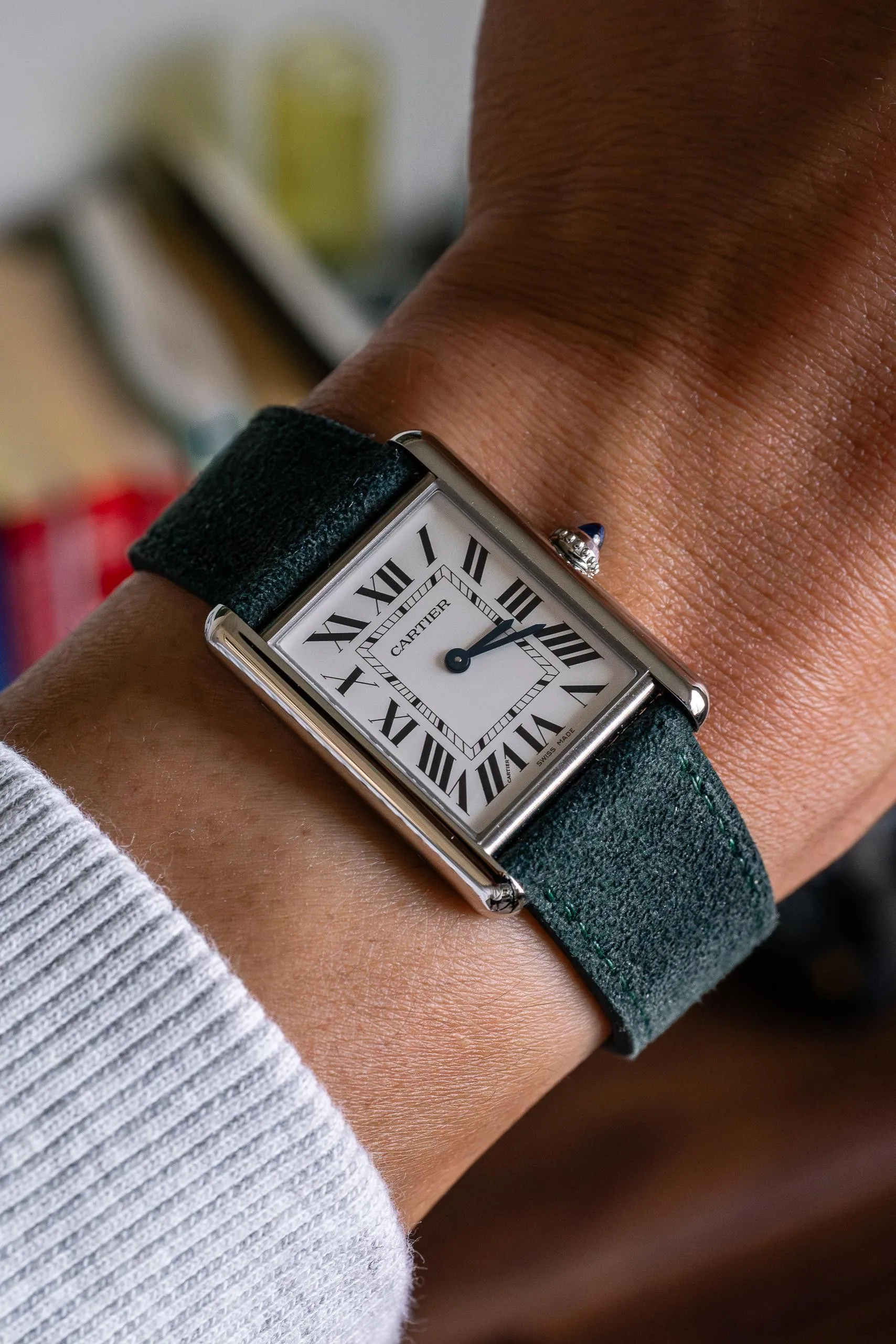 Cartier Tank steel close-up on wrist, white Roman numeral dial, blued hands, green suede strap