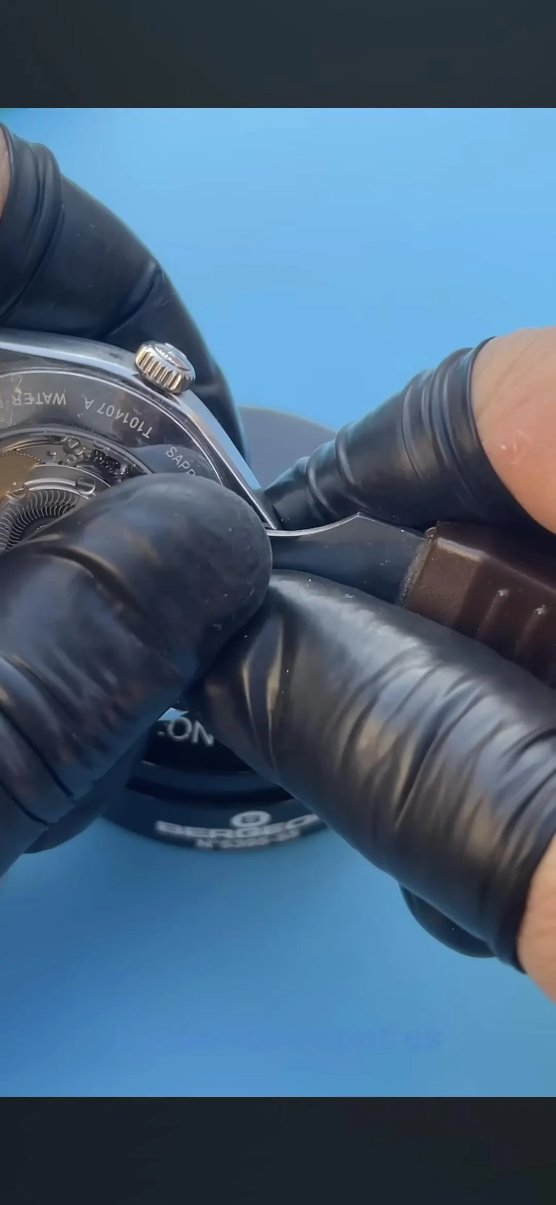 Gloved hands opening Tissot PRX exhibition caseback, movement visible through sapphire window.
