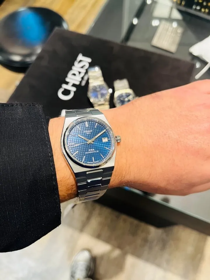 Tissot PRX Powermatic 80 blue dial on wrist, three-quarter angle in boutique setting.