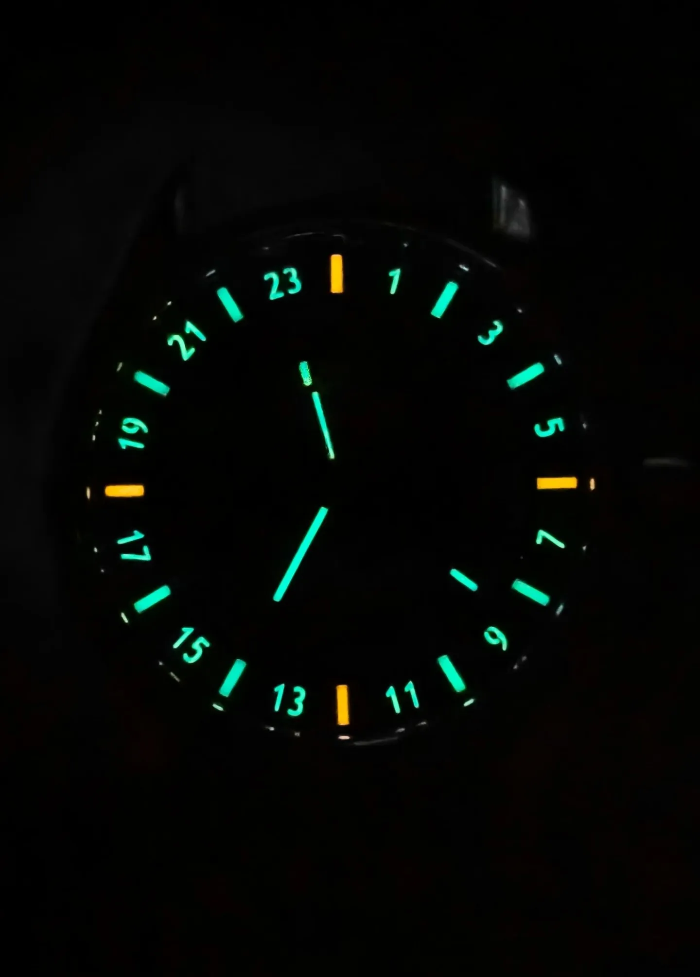 Watch dial glowing in dark with cyan tritium tube markers on 24-hour scale and orange accents